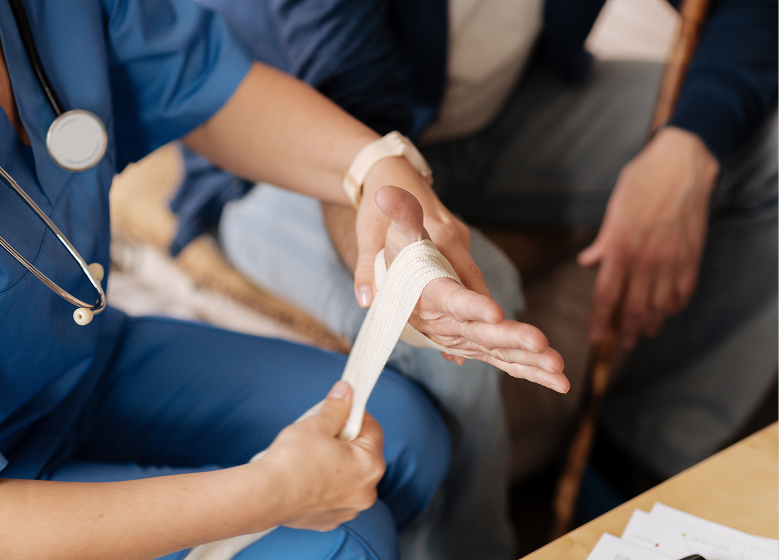 A healthcare professional in blue scrubs wraps a bandage around a patient's hand, suggesting care and empathy. A stethoscope is visible.